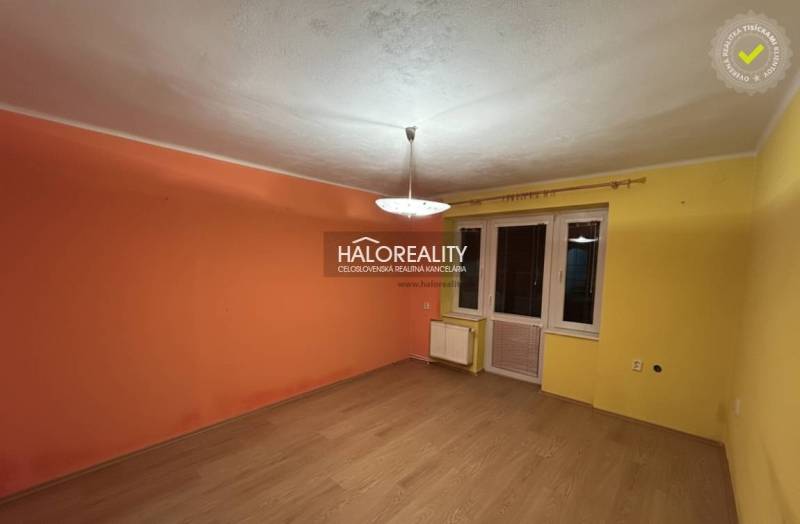 A room in a 2-room apartment with orange-yellow walls and a wooden decor floor.