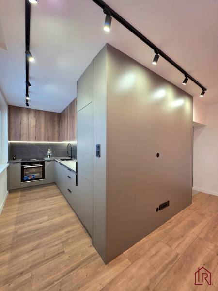 Kitchen area of a 3-room apartment with a wooden decor floor and ceiling track lighting.