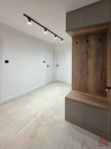 A hallway in a 3-room apartment with white walls, ceramic flooring, and wall cabinets.