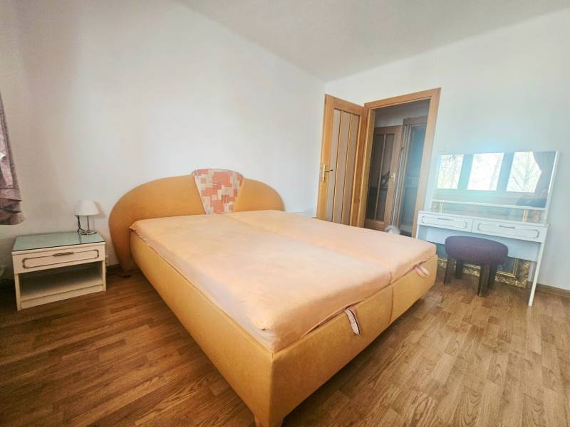 A bedroom with an orange bed, a nightstand, and a wooden decor floor in a three-room apartment.