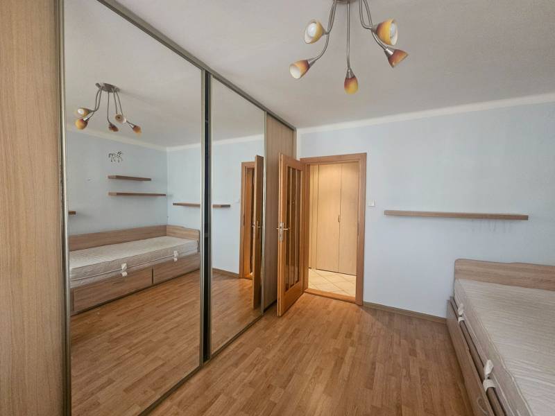 A bedroom in a 3-room apartment with a wooden decor floor and a large mirrored wardrobe.