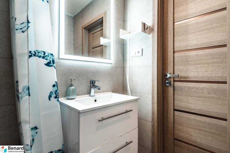 Bathroom with a sink, mirror, patterned curtain, and wooden decor door in a 2-room apartment.