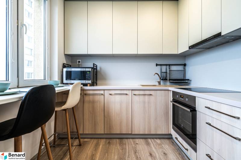A kitchen in a 2-room apartment with a wooden decor floor and light furniture.