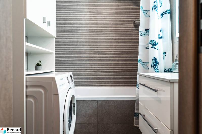 A bathroom in a 2-room apartment with a shower curtain, washing machine, and storage space.