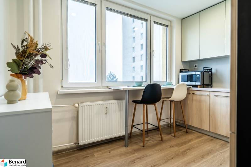 A kitchen in a 2-room apartment with a bar counter, stools, and a floor with a wooden decor.