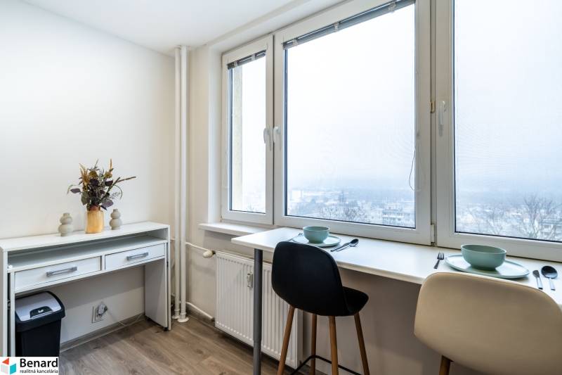 Dining area by the window with a view, two chairs, in a two-room apartment with wood-patterned flooring.