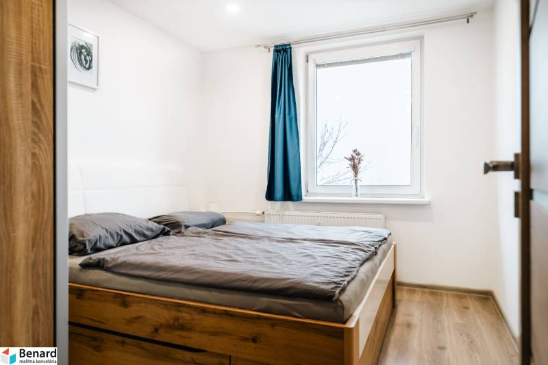 Bedroom with wood-patterned flooring and a bed in a two-room apartment, blue curtain on the window.
