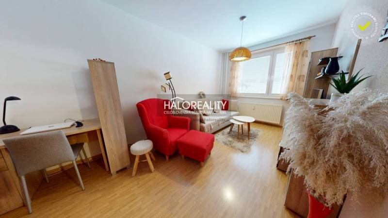 Living room in a two-room apartment with a table, a red armchair, and a wooden-patterned floor.