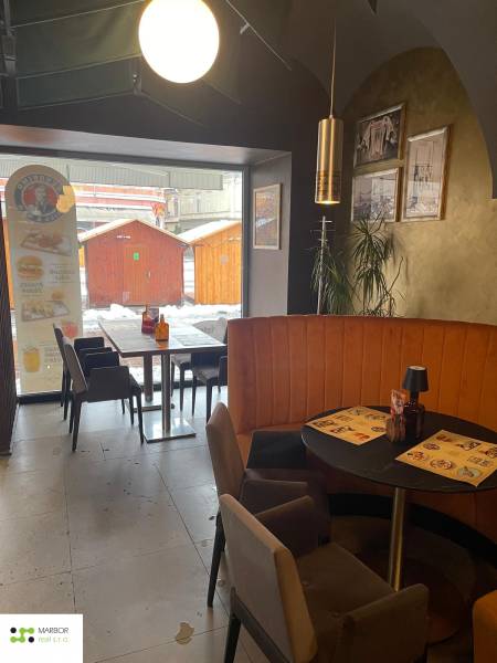Gastro premises with café seating, wall decorations, and a view of wooden stalls outside.