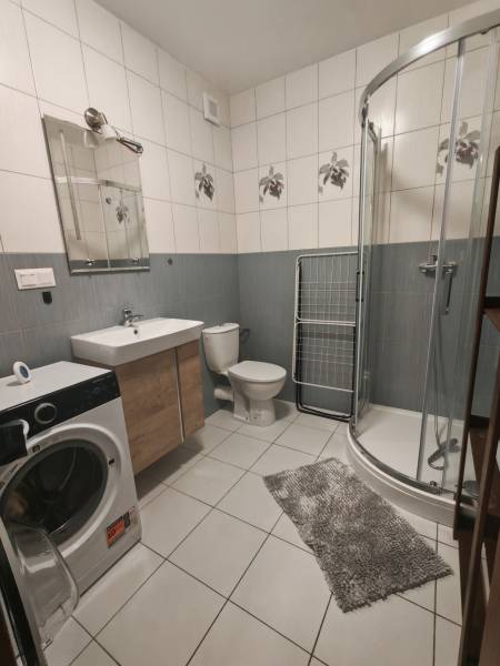 A bathroom in a 3-room apartment with a washing machine, shower corner, and ceramic tiles.