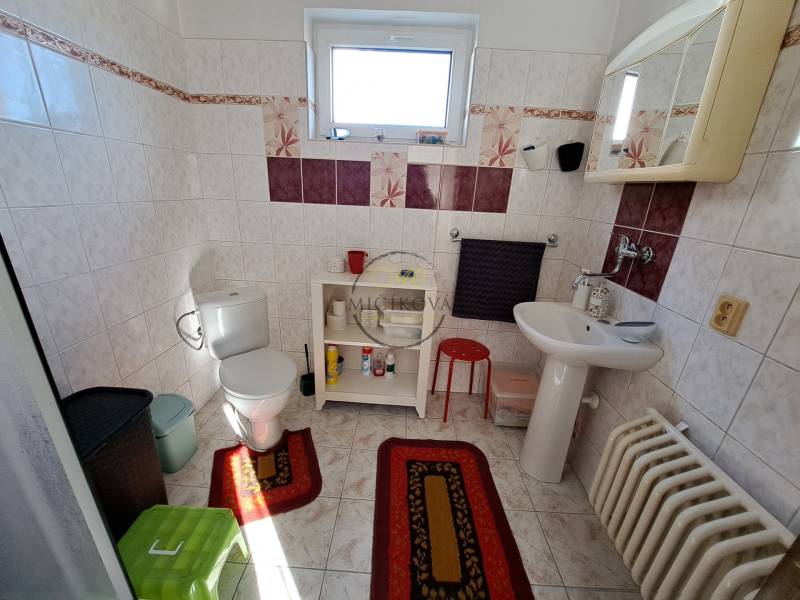 A bathroom with a window in a family house, white sanitary ware, patterned tiles, red rugs.