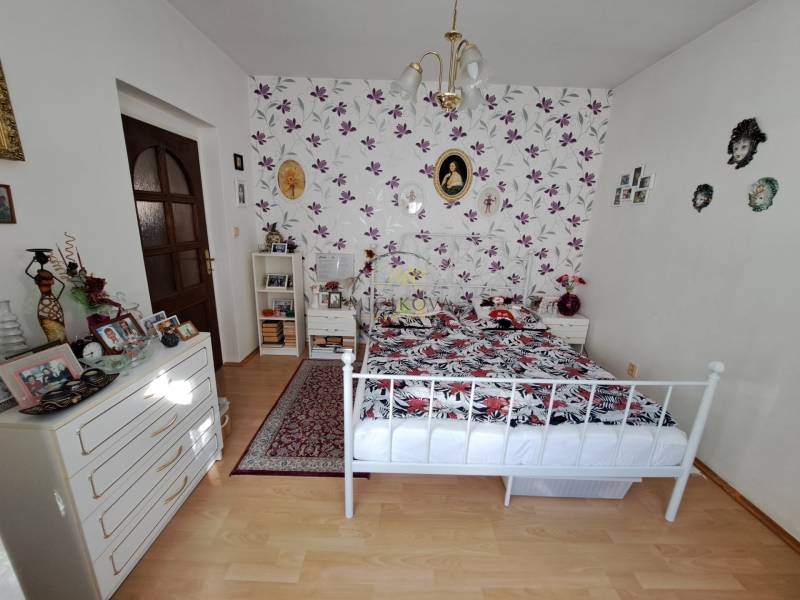 A bedroom in a family house with floral wallpaper, a metal bed, and a wooden decor floor.