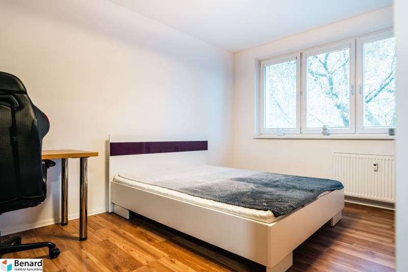 A bedroom with a bed, table, and wooden decor flooring in a two-room apartment.