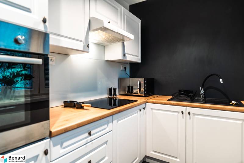 A kitchen in a 2-room apartment with white cabinets and a black wall.