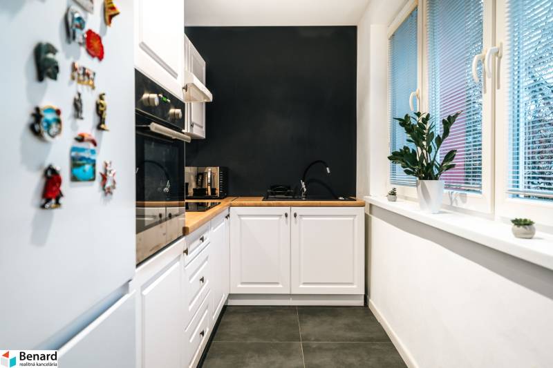 A kitchen in a 2-room apartment with a black wall, wooden decor, and white cabinets.