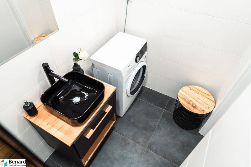 A bathroom in a 2-room apartment with a black sink, a washing machine, and wooden decor.