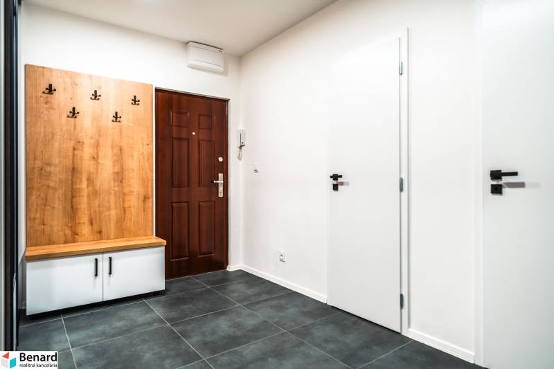 Hallway in a 2-room apartment with tiles, a wooden coat rack, and white doors.