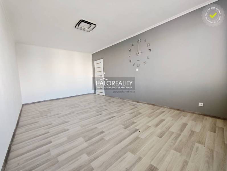 A room with a clock and a wooden decor floor in a two-room apartment.