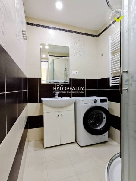 Bathroom with a washing machine and a shower in a 2-room apartment, light tiles, patterned floor tiles.
