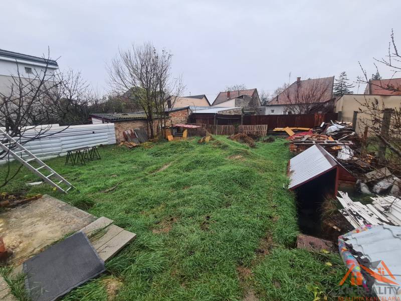 The garden of a family house in Komárno with a lawn, trees, and various materials in the yard.