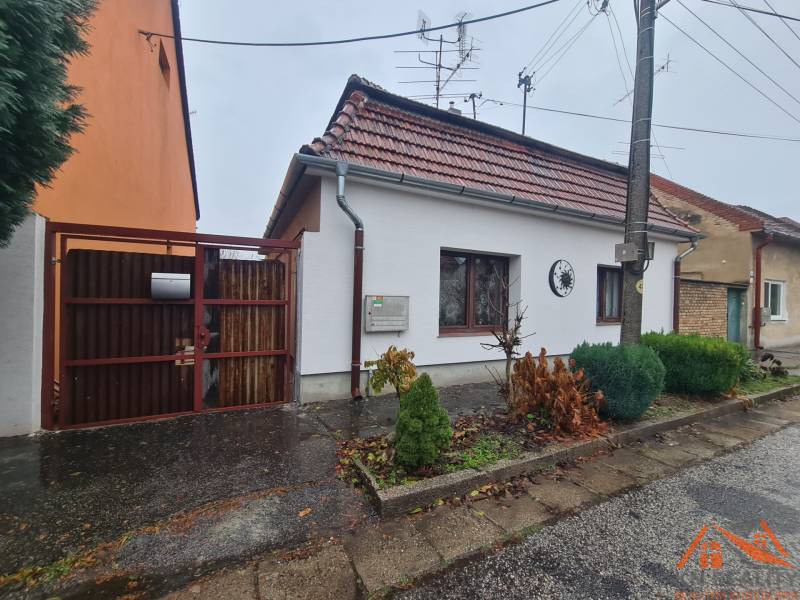 A family house in Komárno with a gable roof and an entrance gate, a front garden with shrubs.