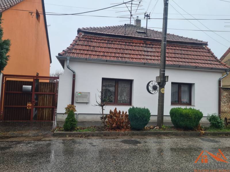 A family house in Komárno with a white facade and a tiled roof, surrounded by greenery.