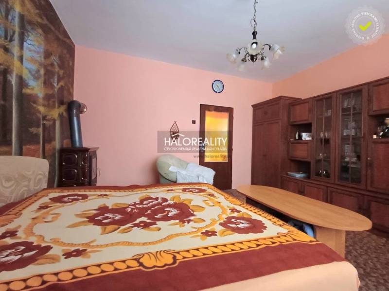 Interior of a family house with wooden furniture, a carpet, and a bed with a colorful throw.