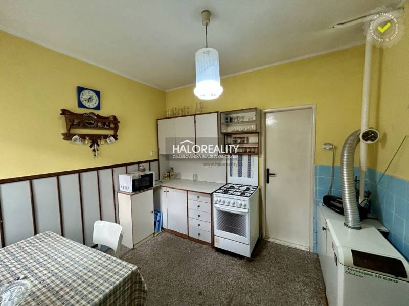 A kitchen in a family house with yellow walls, white furniture, and a carpeted surface.