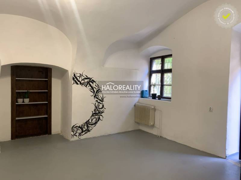 An office interior with white walls, a window, wall decoration, and a wooden shelf.