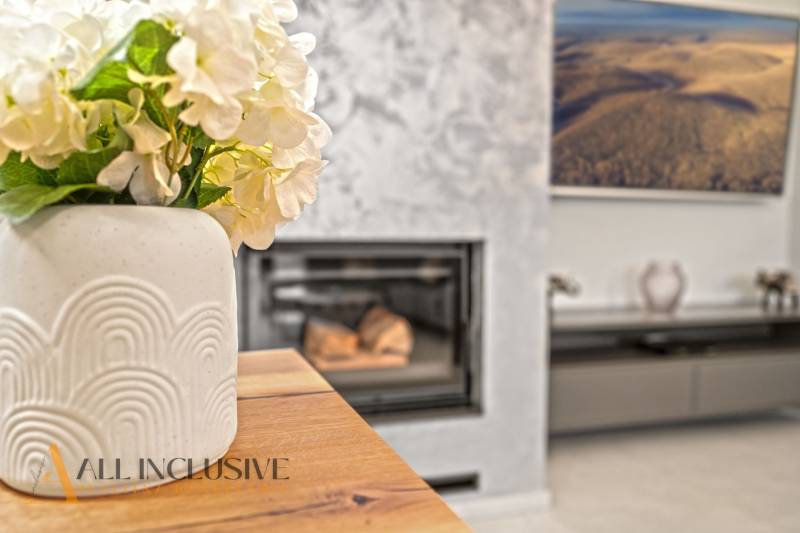 A vase with flowers on the table, a floor with a wooden design, a fireplace in a family house.