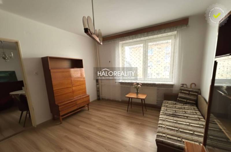 Living room in a three-room apartment with a wooden decor floor, a sofa, a cabinet, and a window.