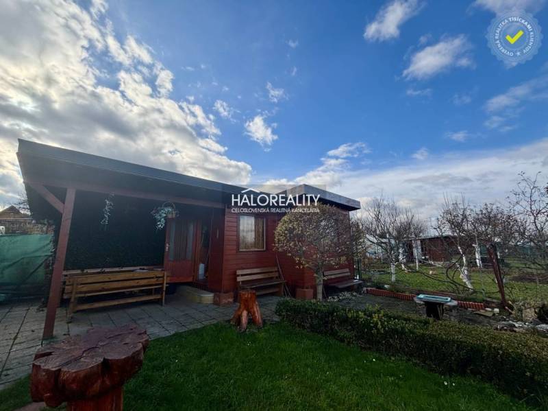 A wooden cottage in the gardens of Spišská Nová Ves with benches and a flower bed.