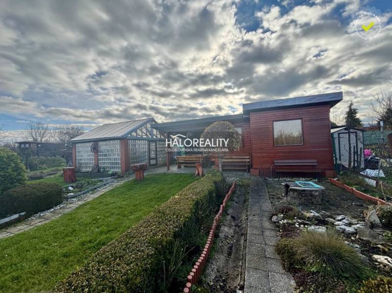 A wooden cottage in the gardens in Spišská Nová Ves, surrounded by a manicured lawn and shrubs.