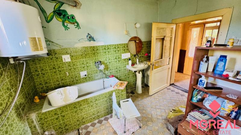 A family house bathroom with a bathtub, green tiles, and a shelf with cosmetics.