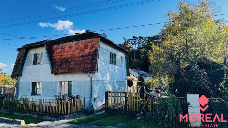 A family house in Brodzany with a wooden fence and a sloped roof, surrounded by greenery.