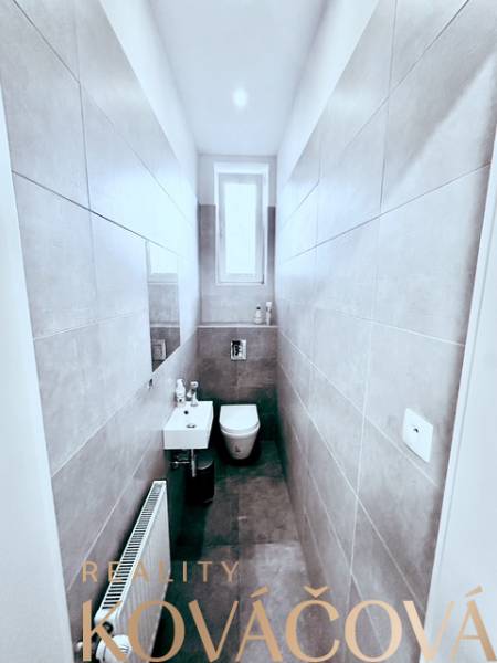 Narrow toilet with a window, sink, and ceramic tiles. Offices Reality Kováčová.