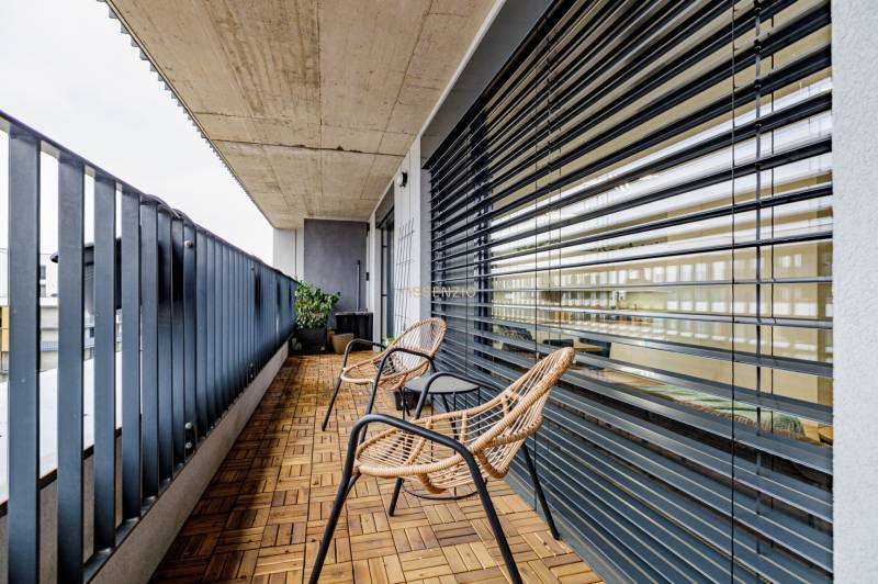 A balcony with a wooden decor floor, rattan chairs, and metal railing.