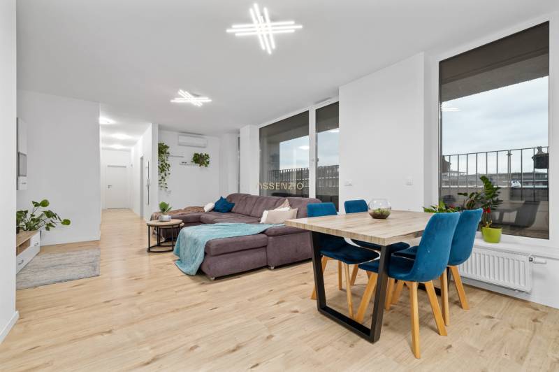 Living room in a three-room apartment with a wooden decor floor, a large sofa, and a dining table.