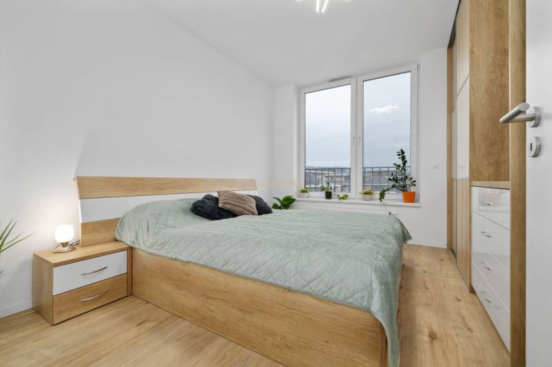 A bedroom in a three-room apartment with a bed, wardrobe, and wooden decor flooring.