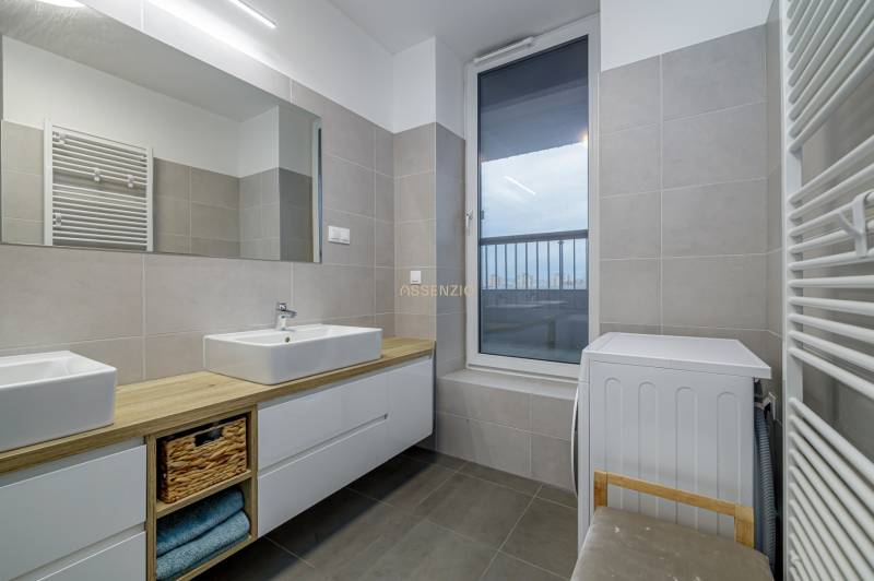 A bathroom in a 3-room apartment with sinks, storage space, a washing machine, and a large window.