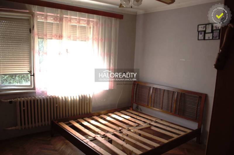 Bedroom in a family house with a bed and a radiator, wooden decor flooring, curtains.