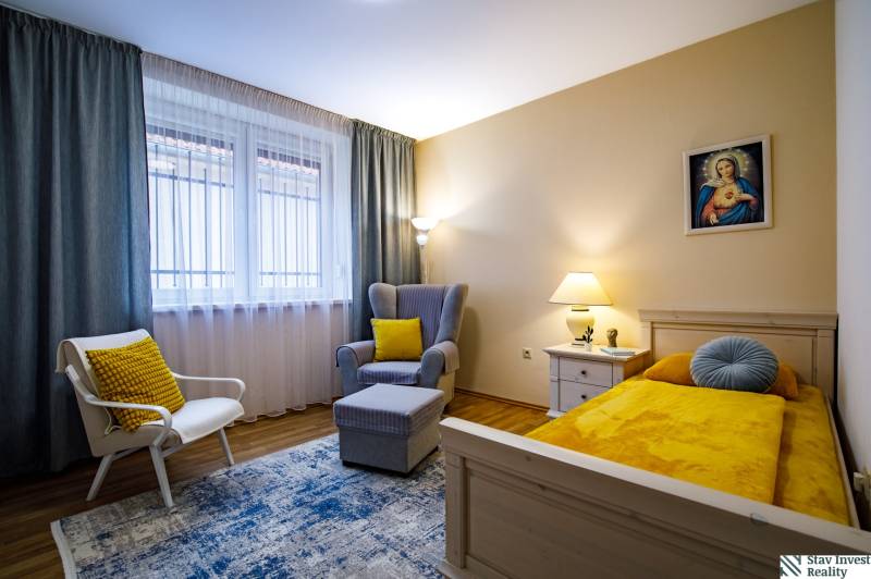 A room in a family house with a bed, a chair, a table, and a floor with a wooden decor.