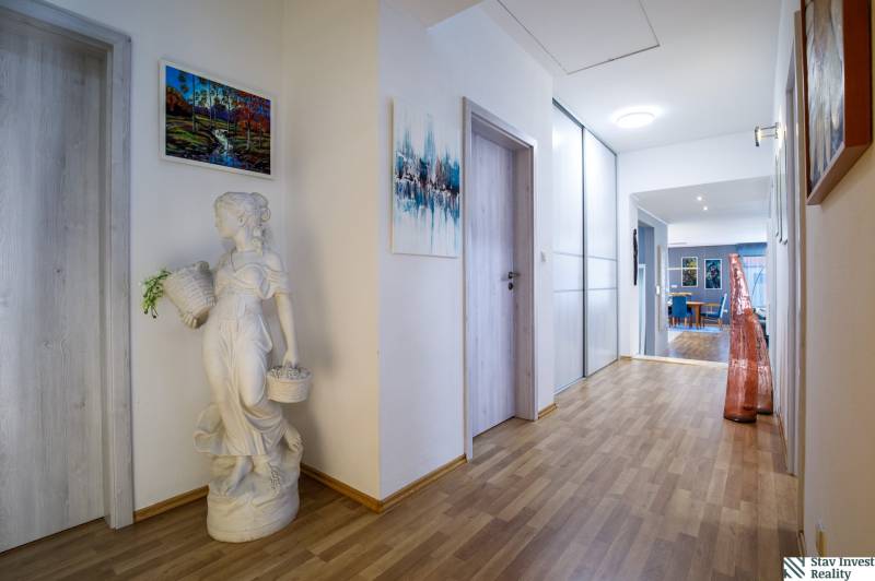 A hallway in a family house with a wooden decor floor, a decorative sculpture, and paintings on the walls.