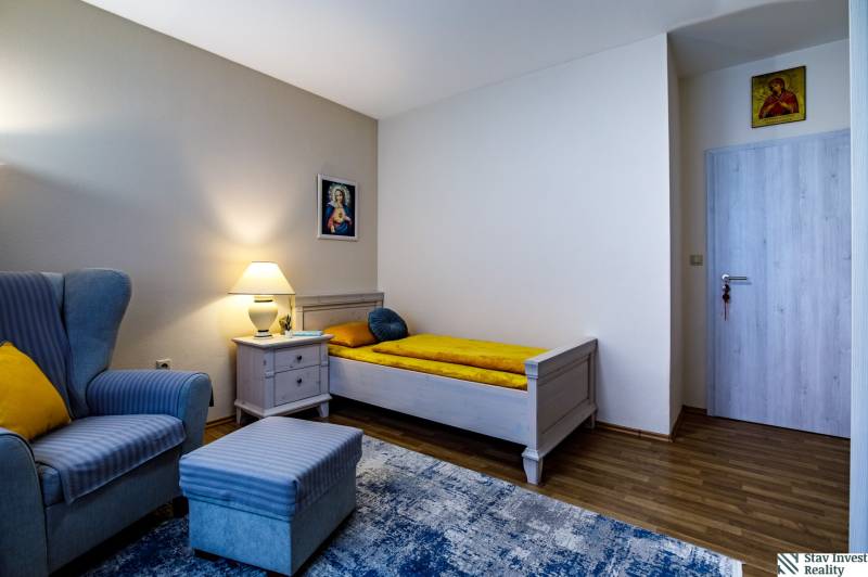 A room in a family house with an armchair, a bed, a nightstand, and a floor with a wooden decor.