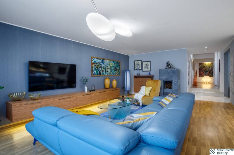 Living room in a family house with a blue sofa, wood-patterned flooring, and a television.