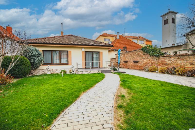 A family house on Školská Street in Senec with a garden, a walkway, and a tower in the background.