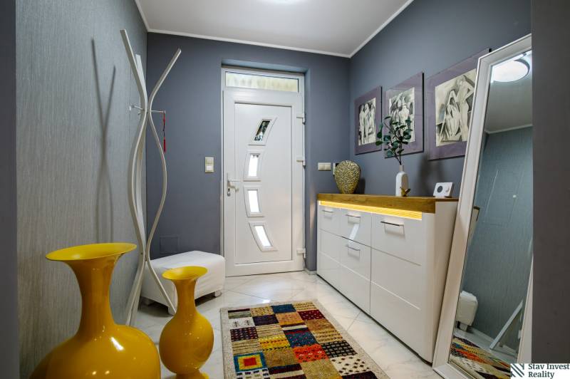 Entrance hall of a family house, white furniture, yellow vases, and a colorful carpet.