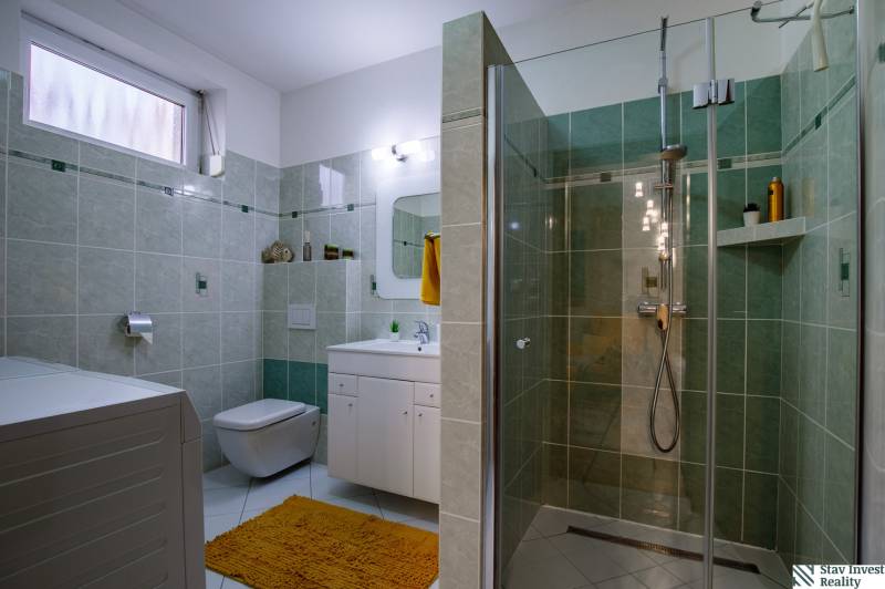 Bathroom with toilet, shower stall, and white cabinets in a family house.