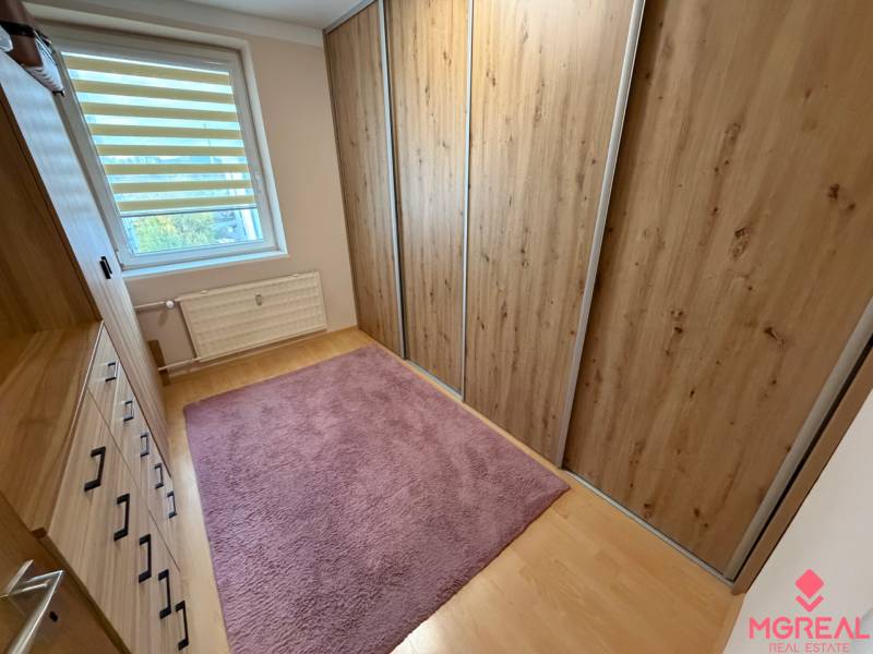 A wardrobe with wooden decor cabinets, a pink carpet, a window with blinds in a 4-room apartment.