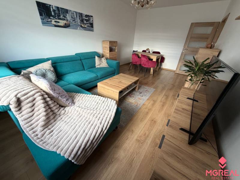 Living room of a 4-room apartment with a turquoise sofa, wooden decor flooring, and a dining table.